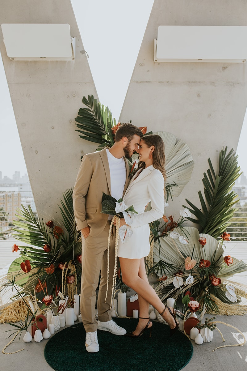 Wedding Photographer, Man and woman lean into each other in front of large arrangement of flowers