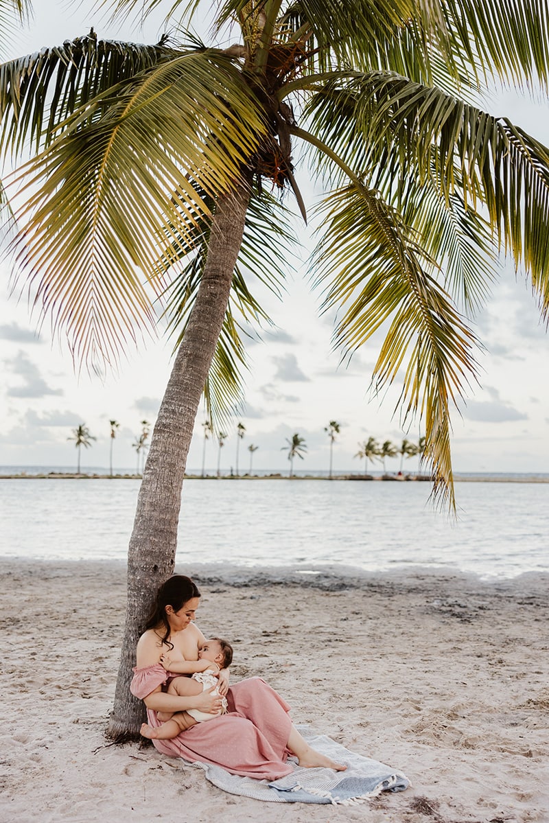 mom breastfeeding baby under palm tree