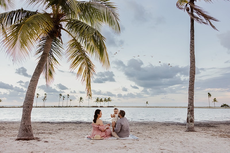 family sitting on a blanket at the beach under palm trees