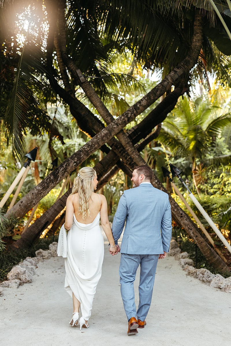 bride, white dress, groom, blue suit, sunrise, beach, sitting on palm tree, under canopy of palm trees