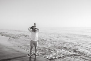 black and white image of dad holding baby at the beach