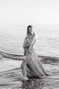 black and white image of mom holding baby at the beach during sunrise