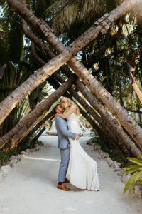 bride, white dress, groom, blue suit, sunrise, beach, sitting on palm tree, under canopy of palm trees